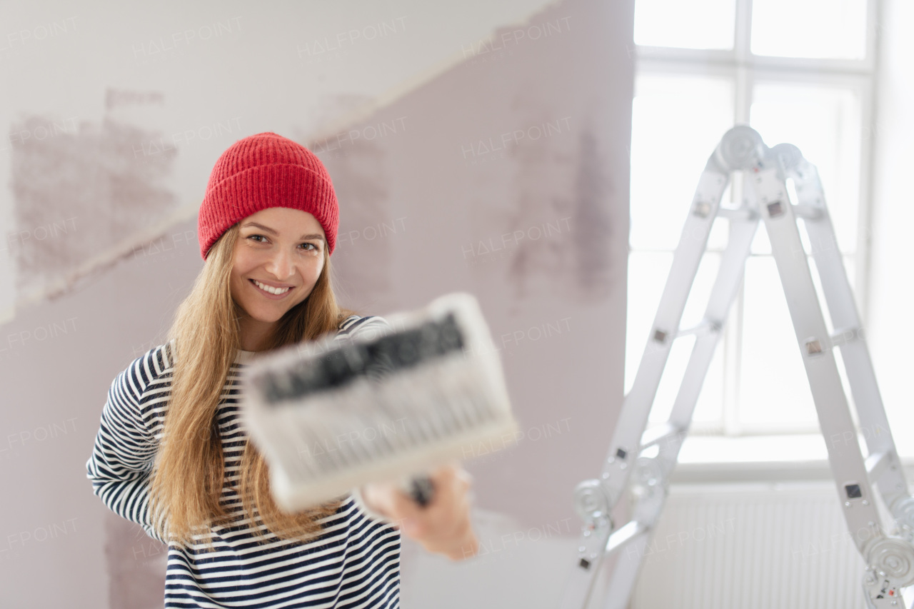 Happy young woman remaking her new house, painting walls. Concept of renovation, indepent women and sustainable lifestyle.