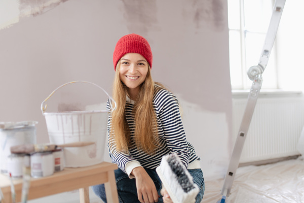 Happy young woman remaking her new house, painting walls. Concept of renovation, indepent women and sustainable lifestyle.