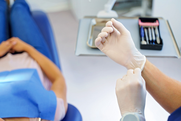 Close up of dentist prepairing for examination of a patient, giving surgical gloves.