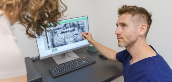 Young dentist showing x-ray scan at computer to patient.