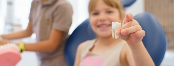 Little girl posing with model of plastic tooth in a dentist ambulance.