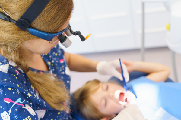 Young woman dentist doing doing preventive examination a little girl.