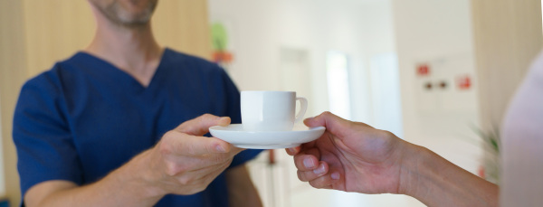 Close-up of dentist giving cup of a coffee to patient, private dental clinic.