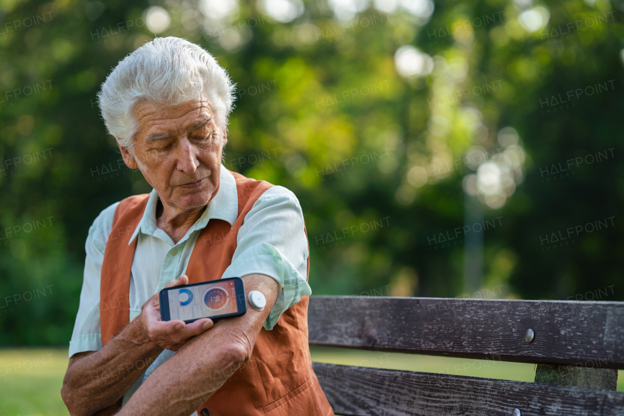 Senior diabetic man checking his glucose data on smartphone. Diabetic senior using continuous glucose monitor to check blood sugar level.