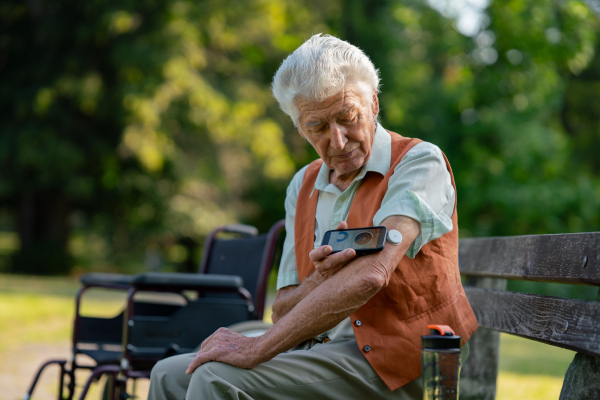 Senior diabetic man checking his glucose data on smartphone. Diabetic senior using continuous glucose monitor to check blood sugar level.