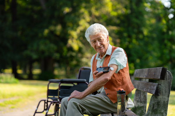 Senior diabetic man in wheelchair checking his glucose data on smartphone. Diabetic senior using continuous glucose monitor to check blood sugar level.