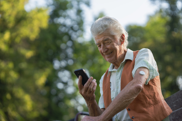 Senior diabetic man checking his glucose data on smartphone. Diabetic senior using continuous glucose monitor to check blood sugar level.