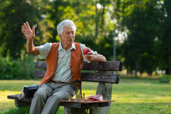 Senior man sitting on a bench, waiting for friend to play chess. An older man with thick hair waving to someone.