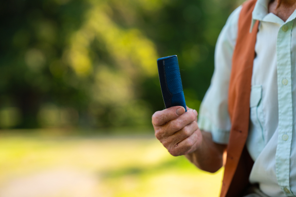 Senior man sitting on a bench in the park and holding comb. Elderly man grooming himself before meeting someone. Older man with healthy, thick hair.