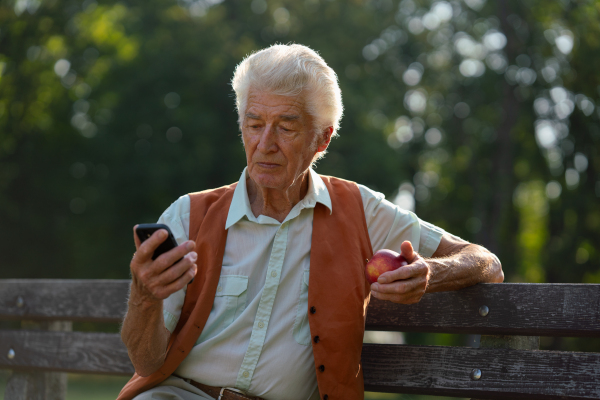 Senior man sitting outside and shopping online on a smartphone. The risk of online shopping scams targeting older people.