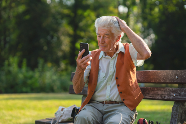 Senior man sitting outside and shopping online on a smartphone. The risk of online shopping scams targeting older people.