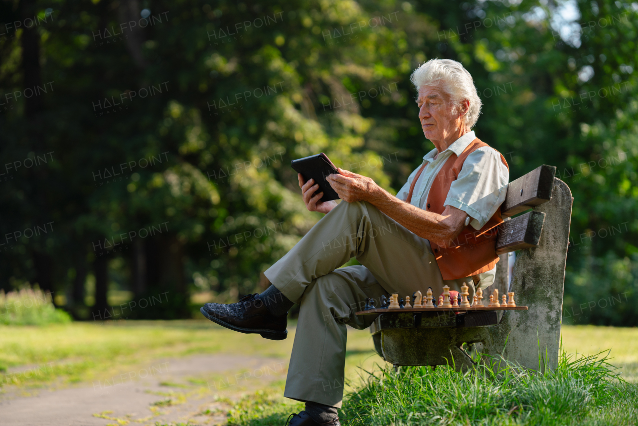 Senior man sitting outside and shopping online on a digital tablet. The risk of online shopping scams targeting older people.