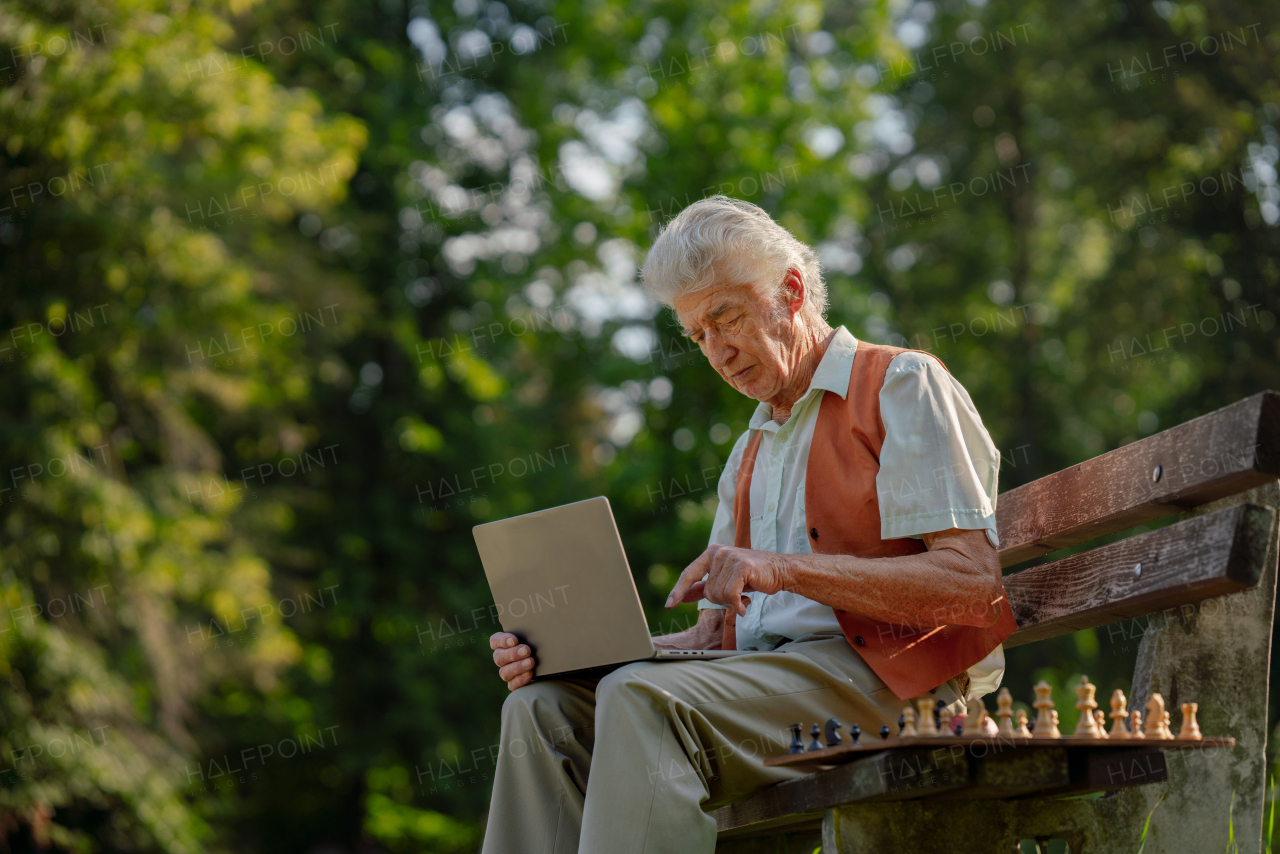 Senior man sitting outside and shopping online on a laptop. The risk of online shopping scams targeting older people.