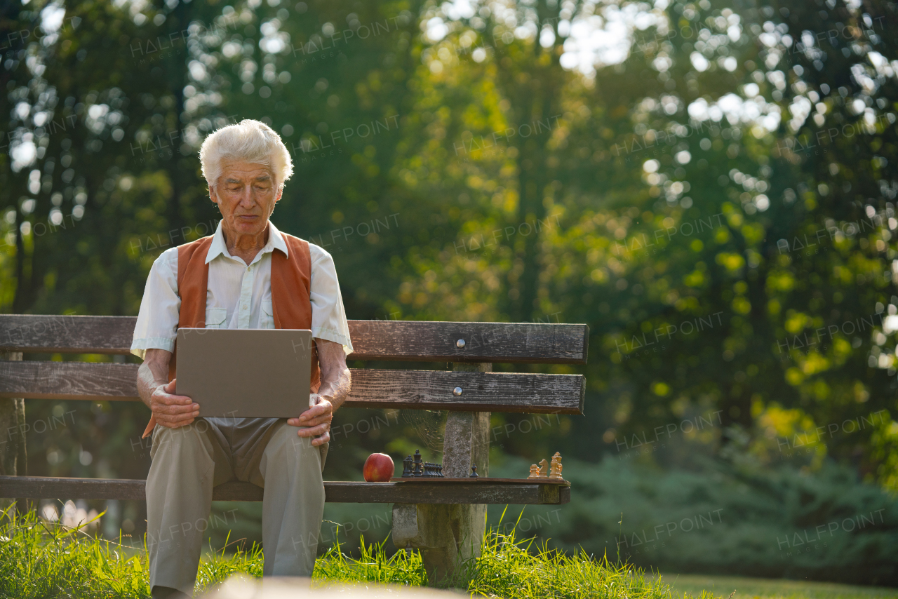 Senior man sitting outside and shopping online on a laptop. The risk of online shopping scams targeting older people.