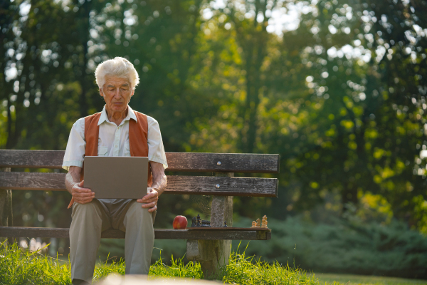 Senior man sitting outside and shopping online on a laptop. The risk of online shopping scams targeting older people.