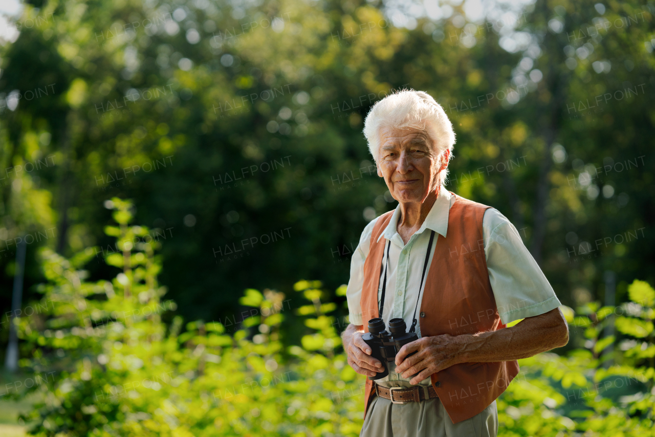 Senior man spending free time outdoors in nature, watching forest animals through binoculars. A retired forest ranger feeling at home in forest, monitoring wildlife and ecological changes.