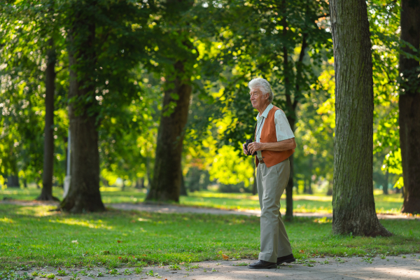 Senior man spending free time outdoors in nature, watching forest animals through binoculars. A retired forest ranger feeling at home in forest, monitoring wildlife and ecological changes.