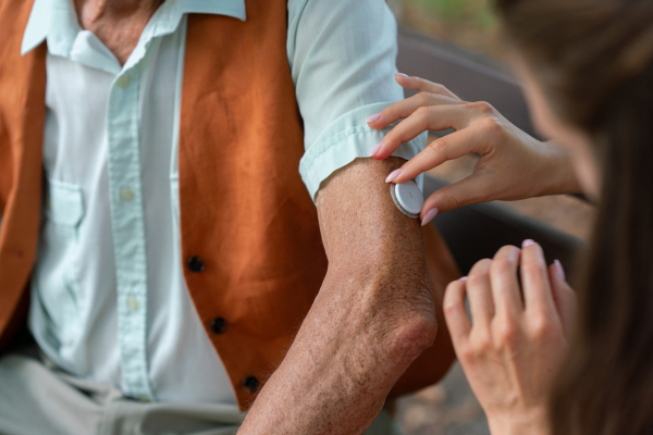 Close up of caregiver helping senior diabetic man to apply continuous glucose monitor sensor on his arm. Diabetic senior using continuous glucose monitor.