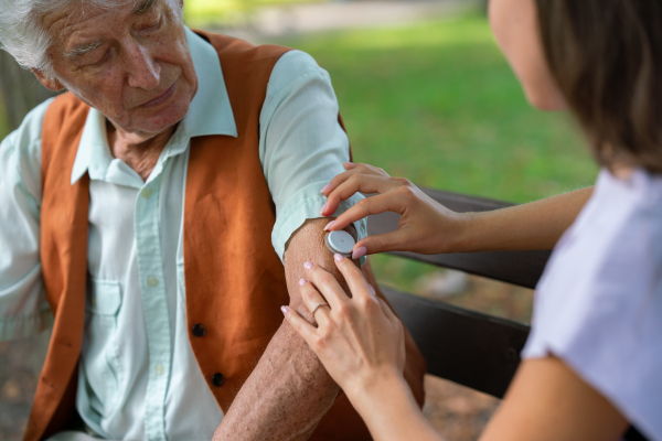 Caregiver helping senior diabetic man to apply continuous glucose monitor sensor on his arm. Diabetic senior using continuous glucose monitor.