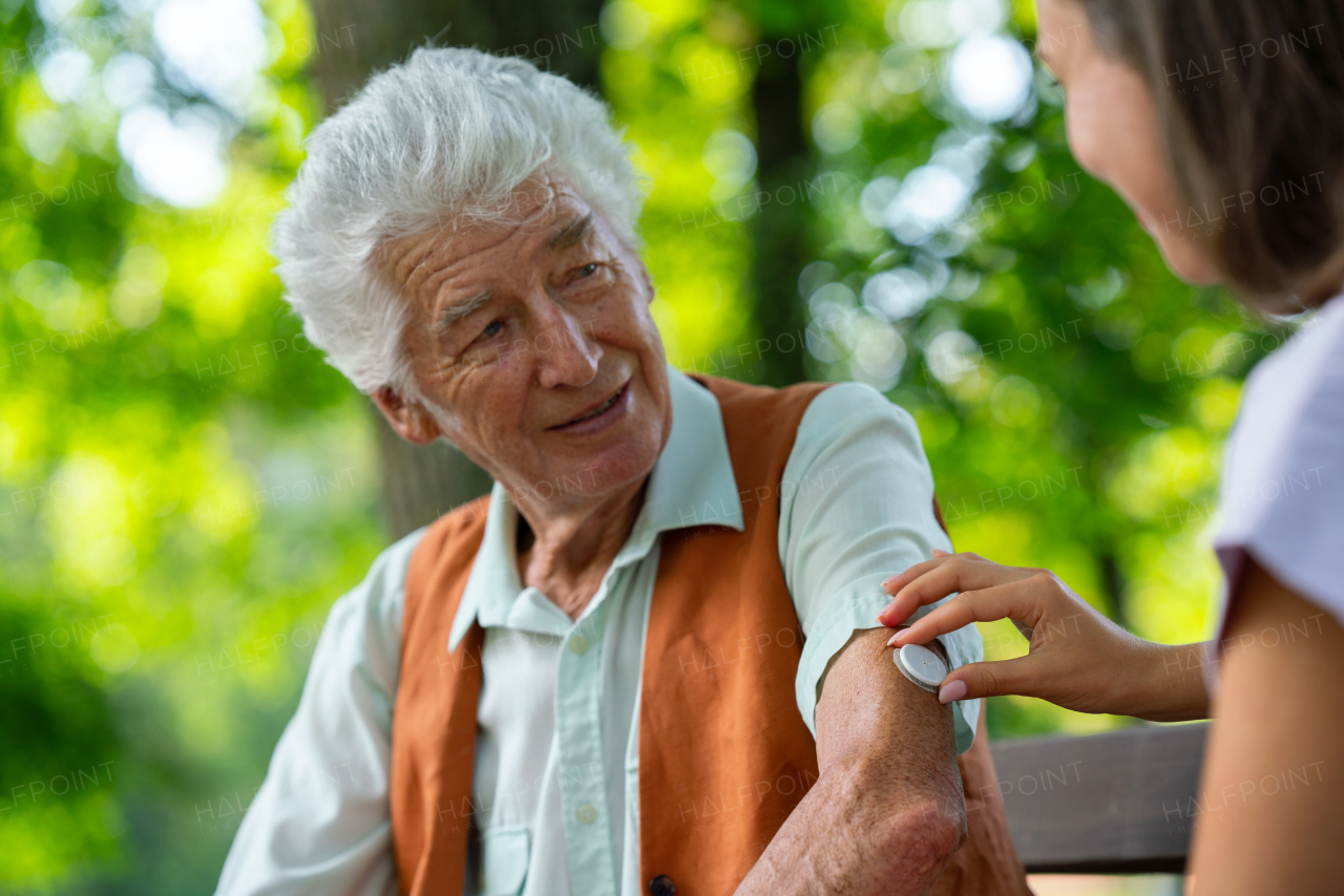 Caregiver helping senior diabetic man to apply continuous glucose monitor sensor on his arm. Diabetic senior using continuous glucose monitor.