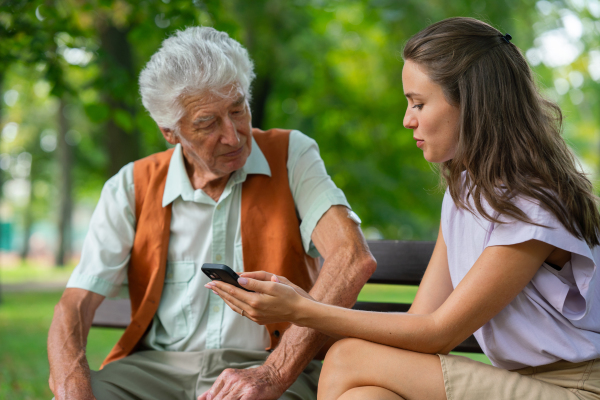 Caregiver helping senior diabetic man check his glucose data on smartphone. Diabetic senior using continuous glucose monitor. Granddaughter teaching her grandfather how to use smartphone, typing texts or browse.