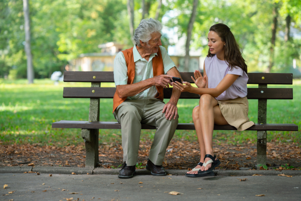 Caregiver helping senior man to shop online on a smartphone. The risk of online shopping scams targeting older people.