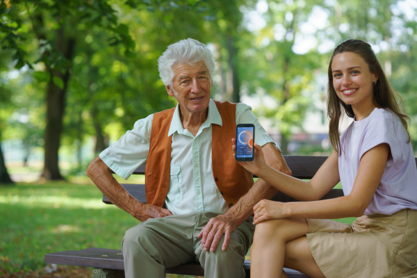 Caregiver helping senior diabetic man check his glucose data on smartphone. Diabetic senior using continuous glucose monitor. Granddaughter teaching her grandfather how to use smartphone, typing texts or browse.