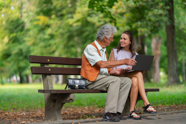 Caregiver helping senior man to shop online on a laptop. The risk of online shopping scams targeting older people.