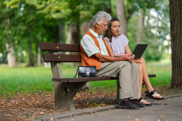 Caregiver helping senior man to shop online on a notebook. The risk of online shopping scams targeting older people.