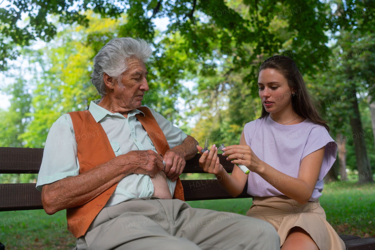 Nurse injecting insulin in belly of diabetic senior patient. Close up of senior man with type 1 diabetes taking insuling with syringe needle in city park. Nurse teaching elderly man how to inject injection himself.