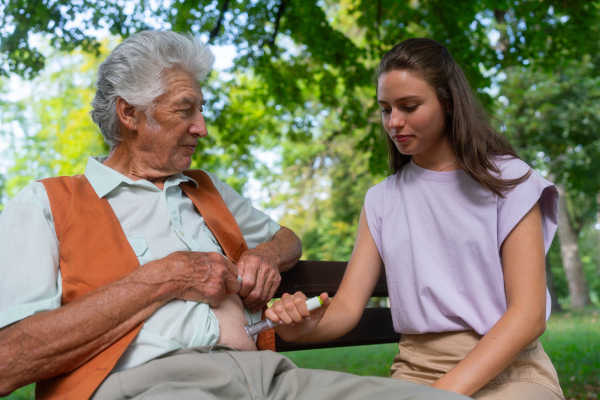 Nurse injecting insulin in abdomen of diabetic senior patient. Close up of senior man with type 1 diabetes taking insuling with syringe needle in city park. Nurse teaching elderly man how to inject injection himself.