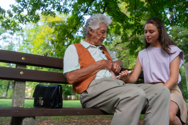 Nurse injecting insulin in abdomen of diabetic senior patient. Close up of senior man with type 1 diabetes taking insuling with syringe needle in city park. Nurse teaching elderly man how to inject injection himself.