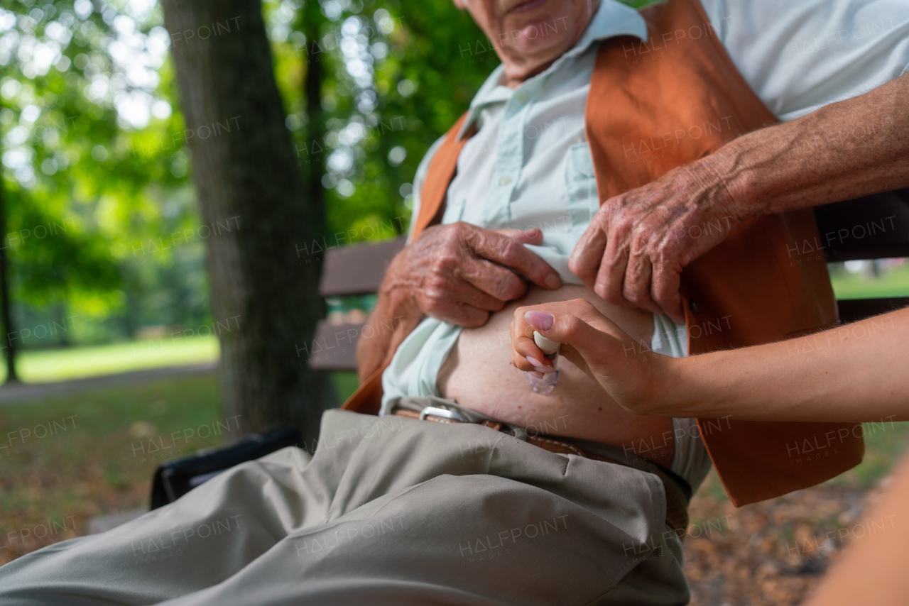 Nurse injecting insulin in belly of diabetic senior patient. Close up of senior man with type 1 diabetes taking insuling with syringe needle in city park. Nurse teaching elderly man how to inject injection himself.