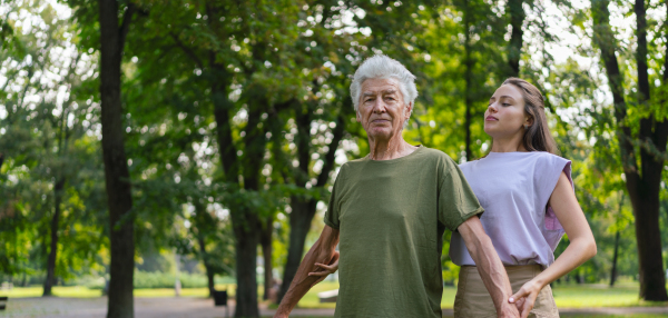 The senior man exercising in the park, A young caregiver showing older man how to perform the exercise correctly. A portrait of a young physiotherapist training outdoors in the park with senior patient. Banner with copy space.