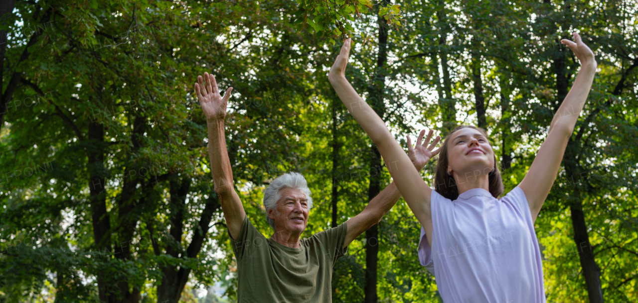 The senior man exercising in the park, A young caregiver showing older man how to perform the exercise correctly. A portrait of a young physiotherapist training outdoors in the park with senior patient. Banner with copy space.