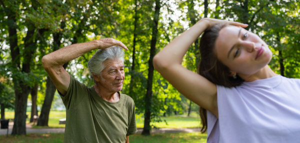 The senior man exercising in the park, A young caregiver showing older man how to perform the exercise correctly. A portrait of a young physiotherapist training outdoors in the park with senior patient. Banner with copy space.