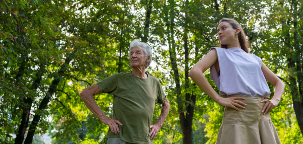 The senior man exercising in the park, A young caregiver showing older man how to perform the exercise correctly. A portrait of a young physiotherapist training outdoors in the park with senior patient. Banner with copy space.