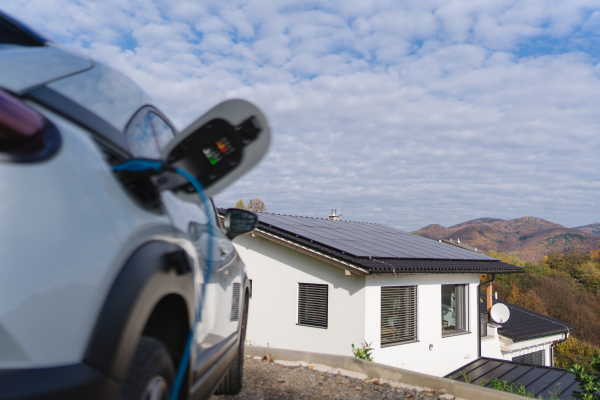 Charging electric car with own charger in house, sustainable transportation concept.