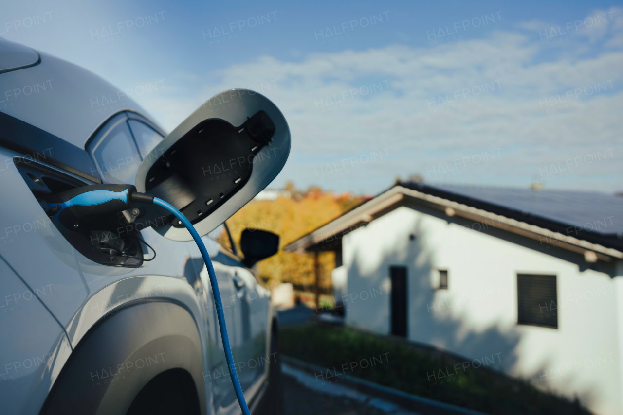 Charging electric car with own charger in house, sustainable transportation concept.