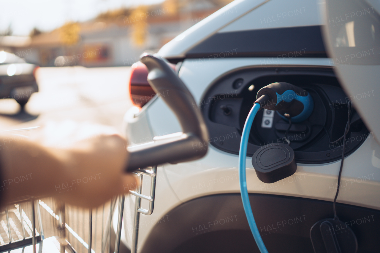 Close-up of charging electric car at supermarket parking.