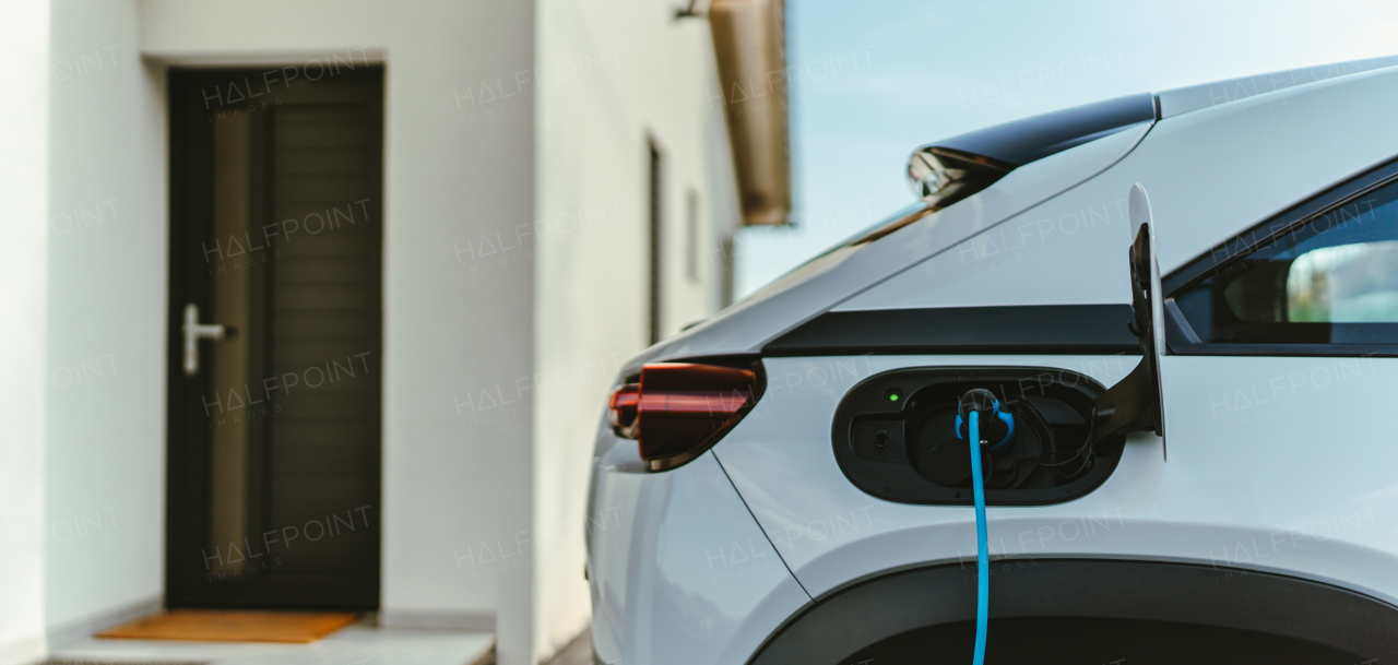 Charging electric car with own charger in house, sustainable transportation concept.