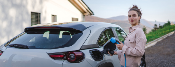 Young woman charging electric car in home, sustainable and economic transportation concept.