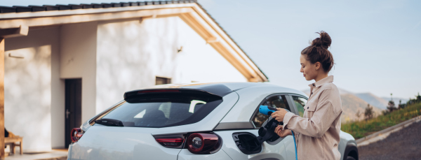 Young woman holding power supply cable from her car, prepared for charging it in home, sustainable and economic transportation concept.