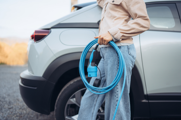 Close-up of woman holding power supply cable from her car, prepared for charging it in home, sustainable and economic transportation concept.