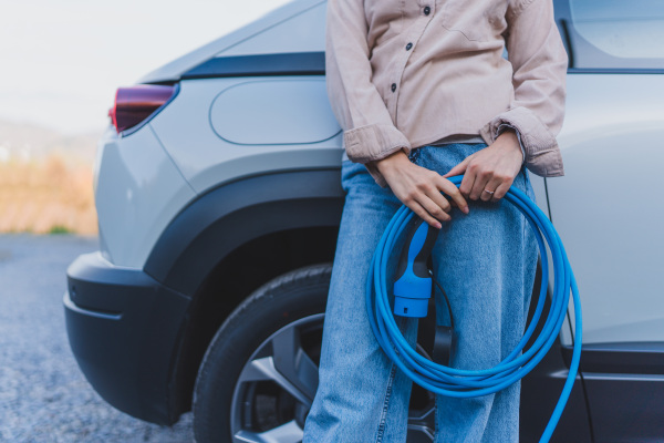 Close-up of woman holding power supply cable from her car, prepared for charging it in home, sustainable and economic transportation concept.