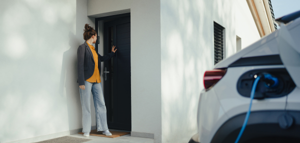 Young woman preparing to work while her electric car charging in own charging station in home, sustainable and economic transportation concept.