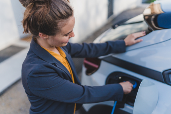 Young woman charging electric car in home, sustainable and economic transportation concept.