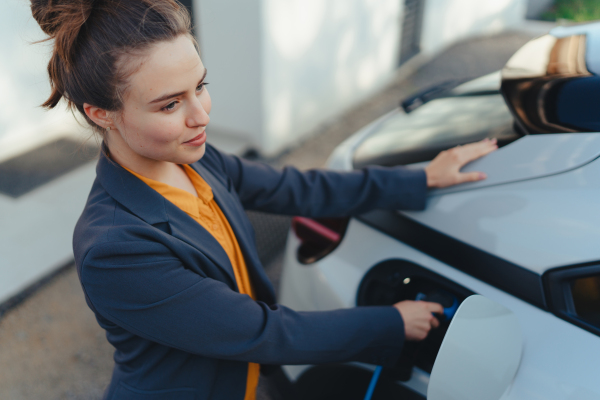 Young woman chargingher car in home, sustainable and economic transportation concept.