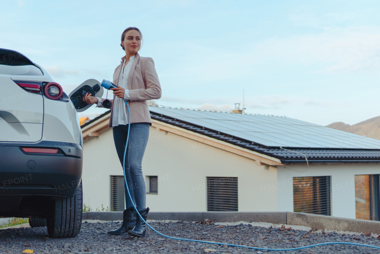 Young woman charging electric car in home, sustainable and economic transportation concept.