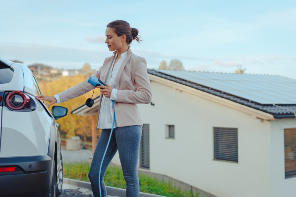 Young woman charging electric car in home, sustainable and economic transportation concept.